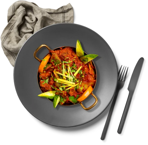 A traditional Indian dish on a plate with utensils and a table cloth